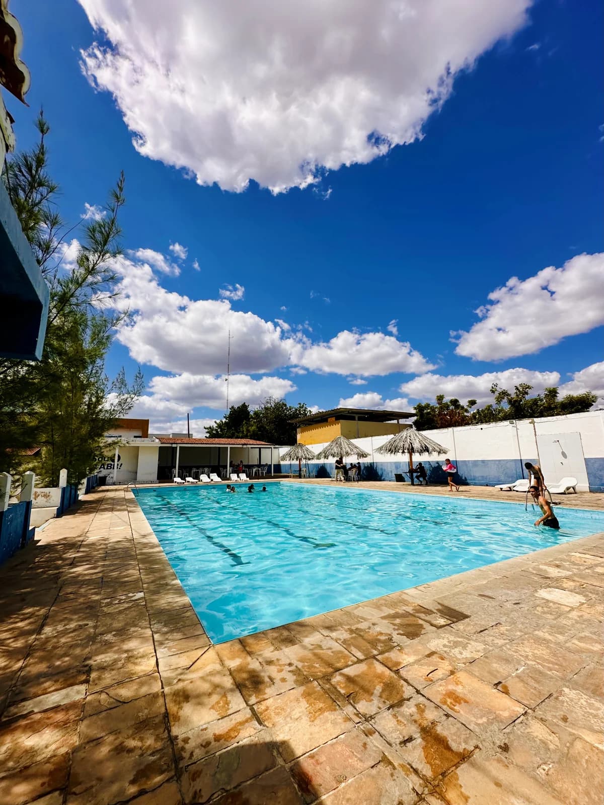 Piscina da AABB Pombal cercada por áreas de lazer, sob um céu azul